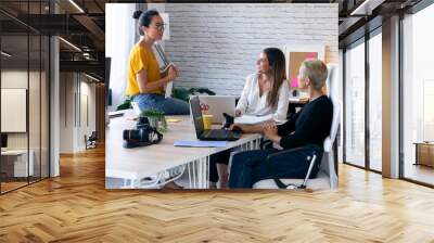 Three modern female entrepreneurs who talk about new ideas for to next work in a joint workspace. Wall mural