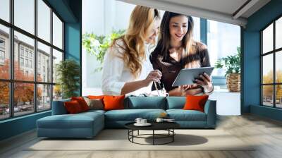 Two attractive young business women working with the digital tablet while talking in a modern office Wall mural