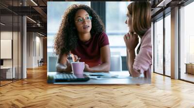 Two beautiful business women working together with laptop while talking about job news in the office. Wall mural