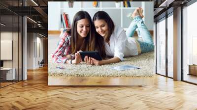 Two beautiful young woman friends using digital tablet at home. Wall mural