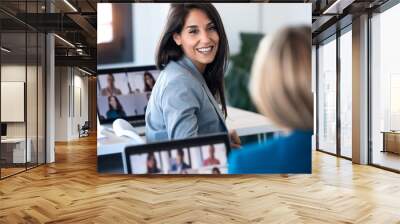 Two business women speaking while doing a video call with diverse colleagues on online briefing with laptop in the office. Wall mural