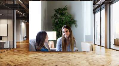 Two happy young female friends conversing in living room at home. Wall mural