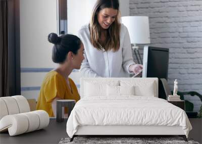 Two young businesswomen talking and reviewing they last work in the digital tablet in the office. Wall mural