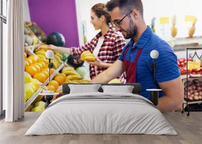 Two young sellers selecting fresh fruit and preparing for working day in health grocery shop. Wall mural