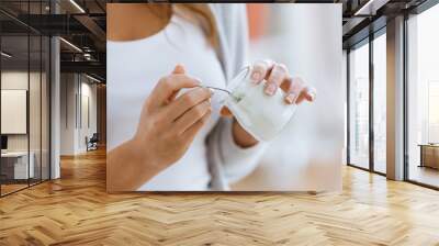 Woman's hand holding yogurt while eating at home. Wall mural