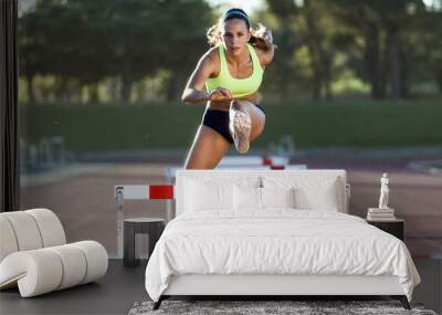 Young athlete jumping over a hurdle during training on race trac Wall mural