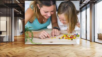 Young mother and daughter playing with sweets at home. Wall mural