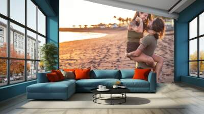 Beautiful lovely young couple on the beach during sunset having fun together, laughing. Real people emotions. Wall mural