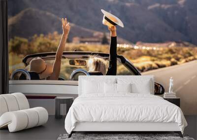 Dreams come true! Two happy young girls driving cabrio car during vacation road trip in mountains, making memories and having fun together. Freedom concept. Happiness. Tourist. Wanderlust. Wall mural