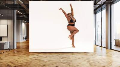 Full photo of happy, wonderful plus size African girl wearing black fashionable swimsuit, laughing and dancing.Concept of body acceptance, body positivity Wall mural