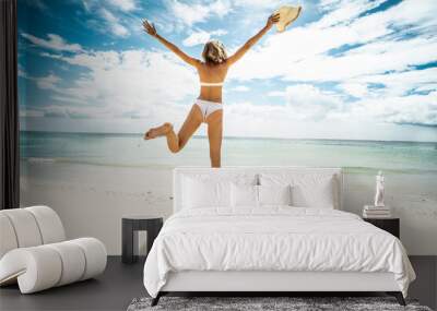 Happy young woman jumping on the beach. Back view. Full length photo. Summer vacation. Traveler. Wall mural