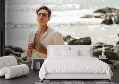 Male model posing in white shirt and eyeglasses on the coast, looking at the camera. Summer vibes. Wall mural