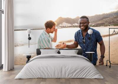 Two handsome multiethnic male friends having a good time together at the beach, smiling, talking, having fun. Summer day. Travelers. Real friendship concept Wall mural