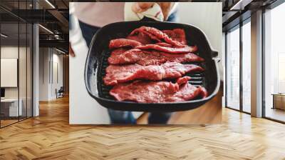 Young man cooking raw meat on grill pan Wall mural