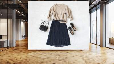 Blue midi pleated skirt, beige knitted sweater, small black cross body bag, belt, loafers (flat shoes) on grey background. Overhead view of women's casual day outfit. Flat lay, top view. Women clothes Wall mural