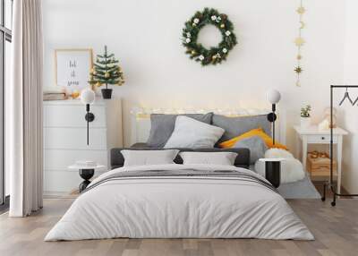 Christmas cozy winter home decor. New year interior decorations. Bed with grey linen, blanket, pillows, plaid, christmas tree, wreath, led garland light, citrus tea on tray. White stylish bedroom. Wall mural