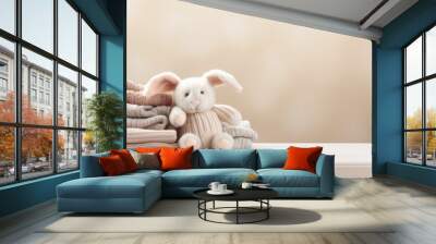 Pile of baby jersey sweaters and textile in beige pastel colors and cute bunny toy Wall mural