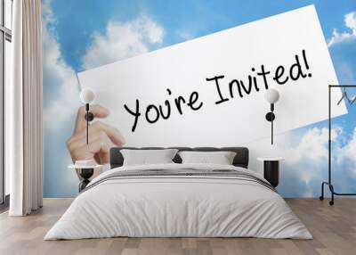 You're Invited! Sign on white paper. Man Hand Holding Paper with text. Isolated on sky background Wall mural