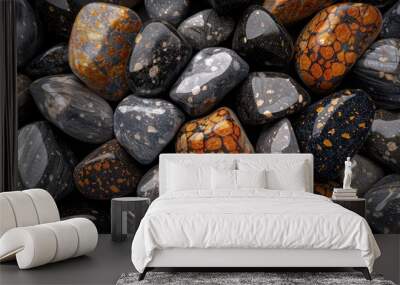 Close-up of a collection of smooth, shiny stones with varying colors and patterns, including clear stones in orange and yellow hues and dark stones with white and yellow flecks. Wall mural