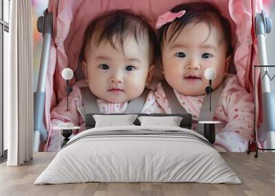 Two little Asian twins wearing pink clothes sit in a pink stroller and look at the camera. Wall mural