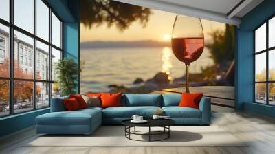 rose wine at sunset. A beautiful sunset view featuring a glass of red wine by the water, creating a serene and romantic atmosphere.  Wall mural