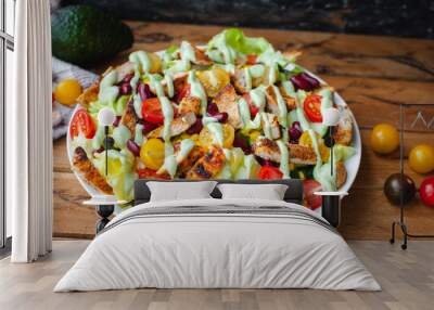 Close-up of chicken salad with fresh vegetables in a plate and avocado dressing, on wooden background Wall mural