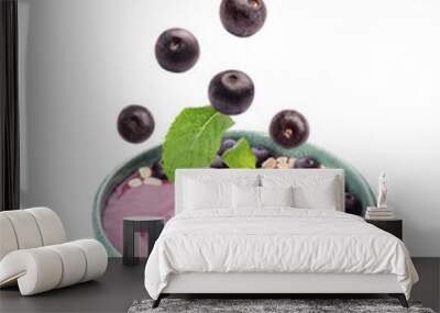 Acai berries and mint falling into bowl on white background Wall mural