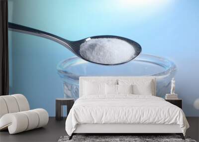 Adding baking soda into glass of water on light blue background, closeup Wall mural