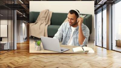 African American man in headphones working on laptop at wooden table in room Wall mural