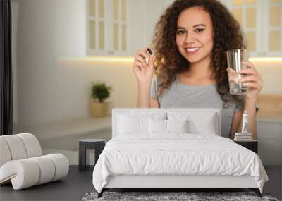 African-American woman with glass of water and vitamin capsule in kitchen. Space for text Wall mural