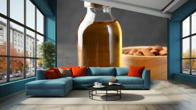 Almond oil in bottle, bowl and nuts on grey textured table, closeup Wall mural