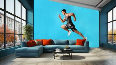 Athletic young man running on light blue background, side view Wall mural