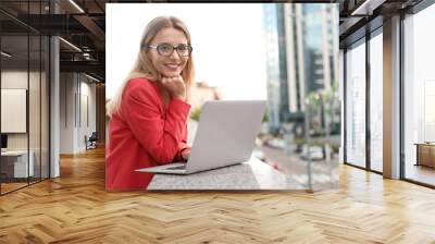 Beautiful businesswoman with glasses using laptop in city Wall mural