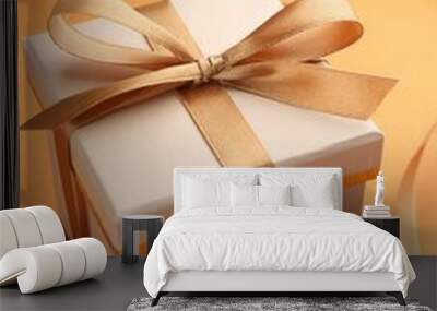 Beautiful gift box with golden bow on orange background, closeup Wall mural