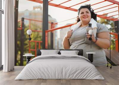 Beautiful overweight woman with towel and bottle on sports ground Wall mural