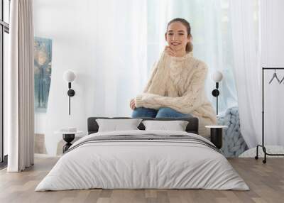 Beautiful teenage girl in warm cozy sweater sitting near window at home Wall mural