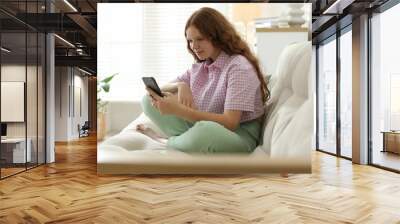 Beautiful teenage girl using smartphone on sofa at home Wall mural