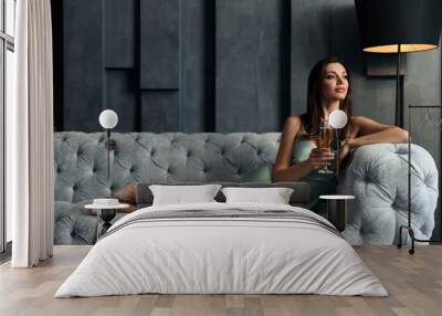 Beautiful woman in elegant dress with glass of champagne on sofa indoors. Luxury lifestyle Wall mural