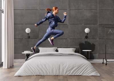 Beautiful woman in gym clothes jumping near dark grey wall on street, space for text Wall mural