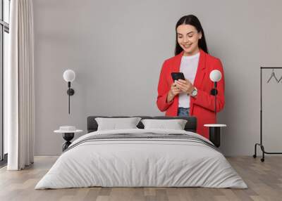 Beautiful woman in red jacket using smartphone on gray background, space for text Wall mural