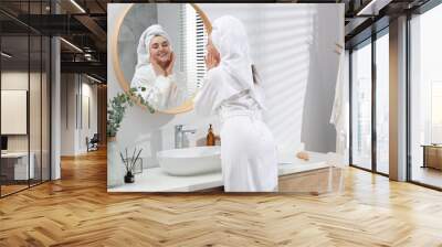 Beautiful woman in white robe applying cream near mirror in bathroom Wall mural