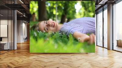 Beautiful woman lying on green grass in park. Spring sunny day Wall mural