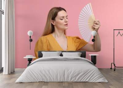 Beautiful woman waving yellow hand fan to cool herself on pink background Wall mural