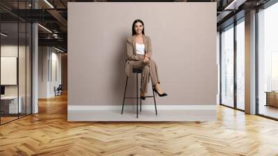 Beautiful young businesswoman sitting on stool near beige wall Wall mural