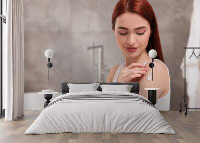 Beautiful young woman applying body cream onto shoulder in bathroom, space for text Wall mural