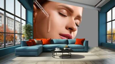 Beautiful young woman applying cosmetic serum onto her face on grey background, closeup Wall mural