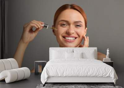 Beautiful young woman applying cosmetic serum onto her face on grey background Wall mural