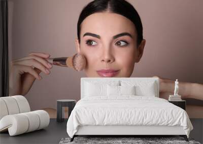 Beautiful young woman applying face powder with brush on dusty rose background Wall mural