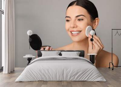 Beautiful young woman applying face powder with puff applicator on grey background Wall mural