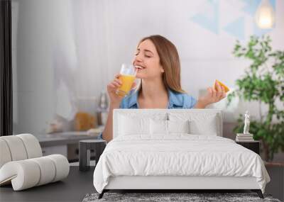 Beautiful young woman drinking fresh orange juice in kitchen. Healthy diet Wall mural